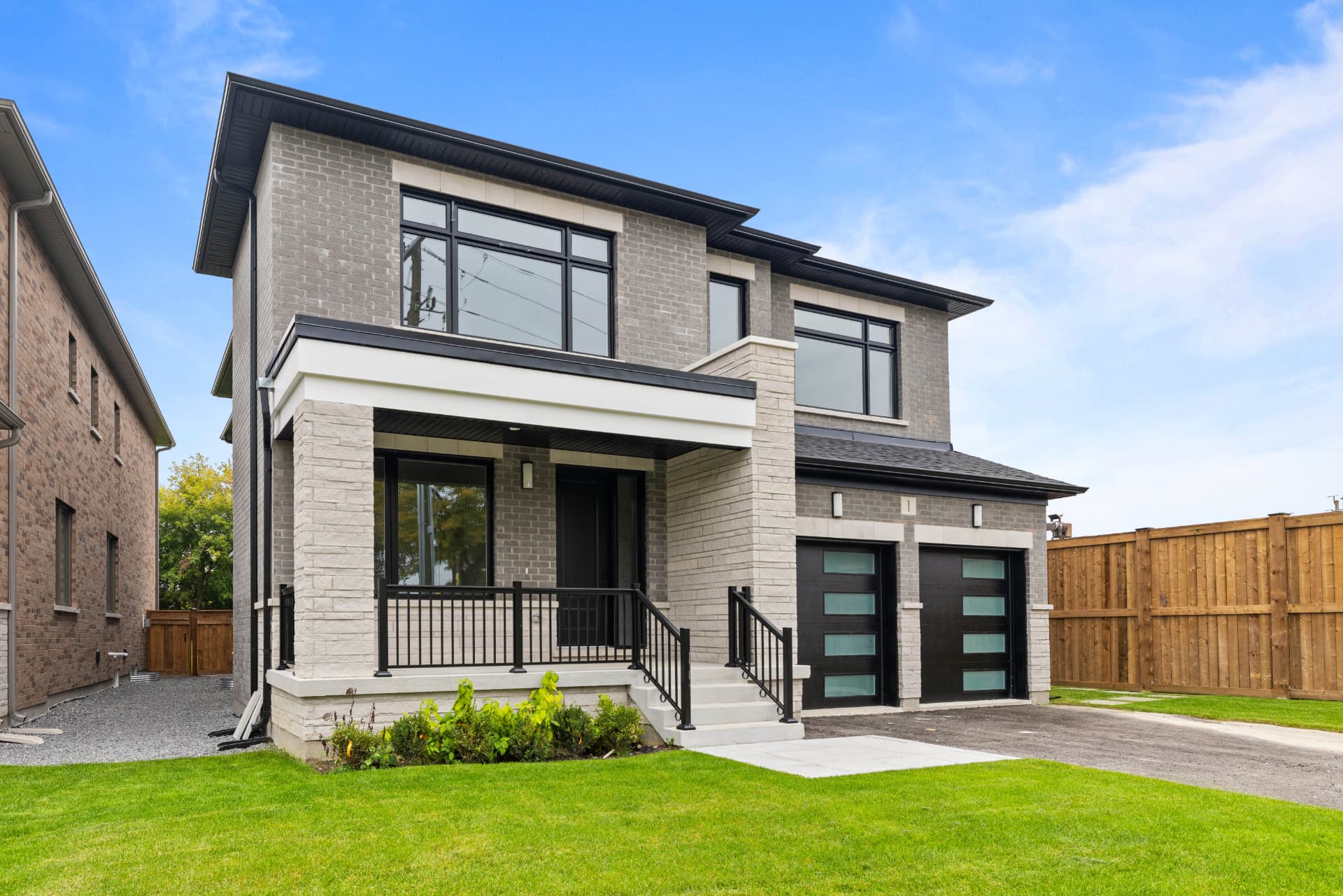 Front exterior with grey brick, stone porch and black double garage doors