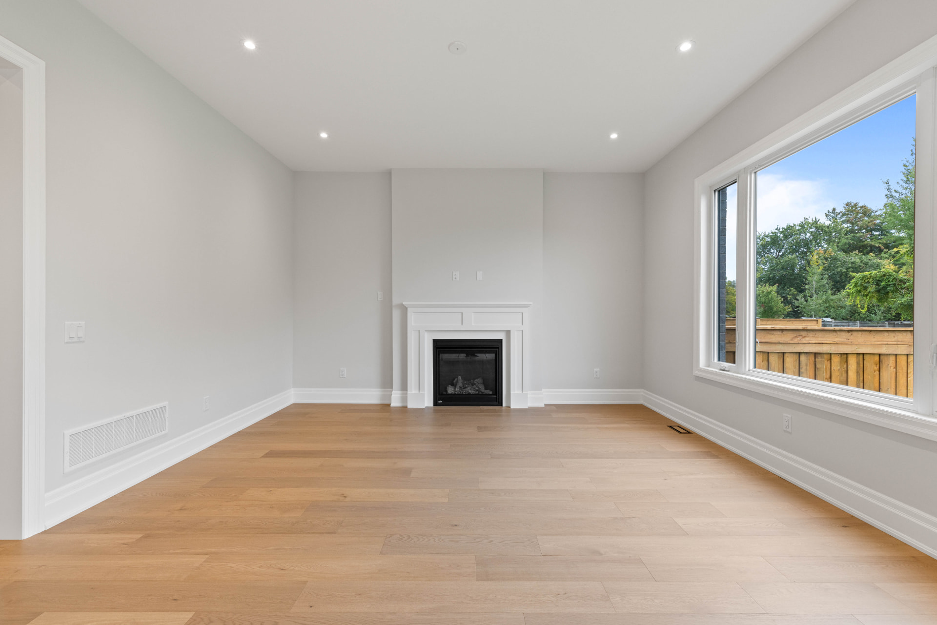 Living room with panelled gas fireplace, oak floors and garden window