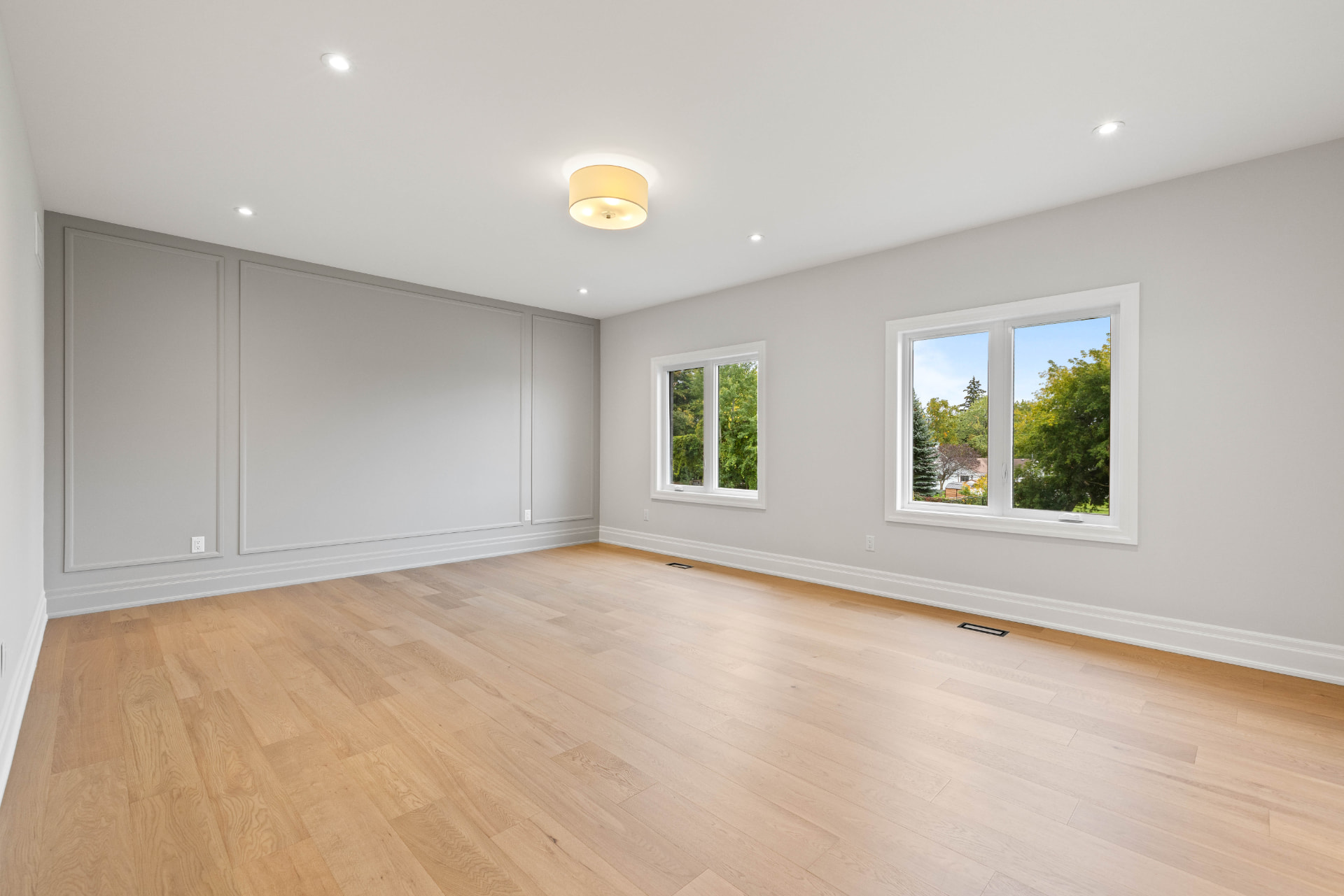 Primary bedroom with grey panelled feature wall, two windows and oak floors