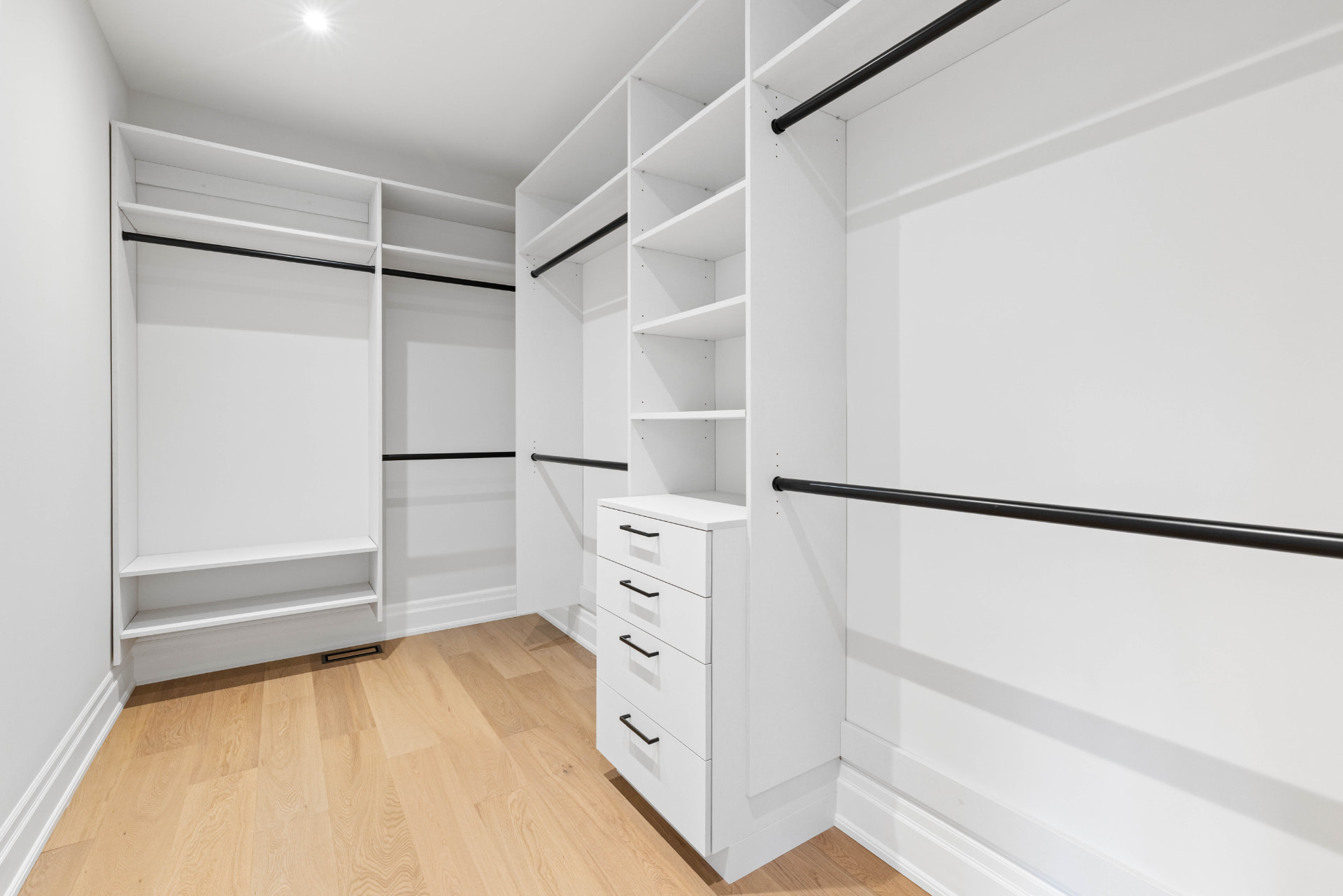 Walk-in closet with custom shelving, black hanging rods and drawer tower